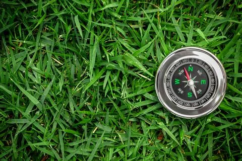  Traditional silver compass with red arrow on green grassy background with space Stock Photos