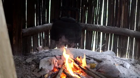 A traditional soot-covered black kettle suspended over campfire embers Stock Footage 337374151