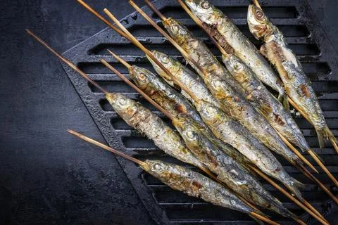 Traditional Spanish barbecue sardines on a wooden skewer as top view on a gri Stock Photos