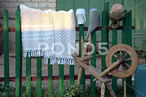 Traditional spinning wheel in Lithuania near green wooden fence with spined Stock Photos