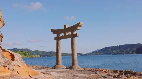 Traditional stone Torii gate standing on coastal rocks overlooking calm ocean Video stock 340749749