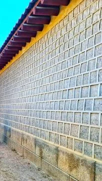 Traditional stone wall featuring square patterns with wooden roofing extendin Фото