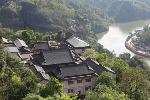 Traditional tiled rooftops on a forested hillside above a winding green river Stock Photos