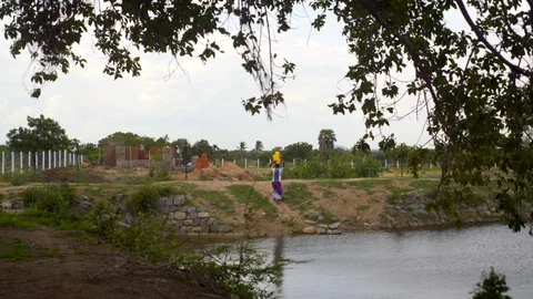 Traditional village woman carries water from lake waterhole, rural IndiaStock Footage