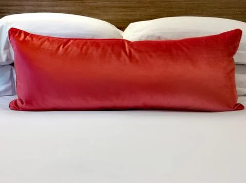Traditionally dressed bed with orange red coloured double velvet cushion Stock Photos