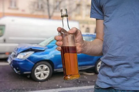 Traffic accident and alcohol concept. Drunk driver is holding bottle with alc Stock Photos