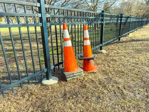 Traffic cones are placed next to a fence in a park area during daytime in a.. Fotos de archivo
