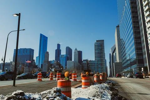 Traffic cones line the road while workers engage in construction in a busy ar Stock Photos