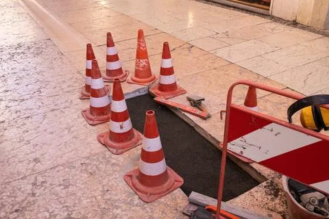Traffic cones placed around an open manhole, warning of potential danger due Stock Photos
