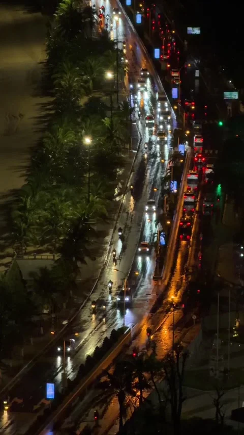 Traffic flows through a lit beachfront avenue while dark waves reach the shore Stock Footage 324839105