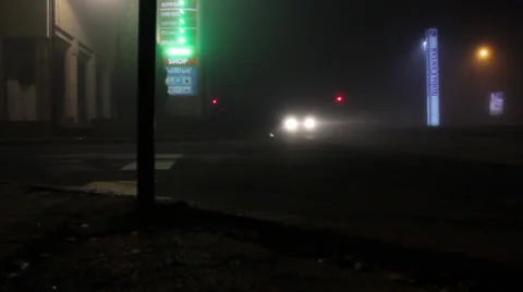 Traffic in a foggy night.Vehicles passing a crossroad.Neon signs at gas station. Stock Footage