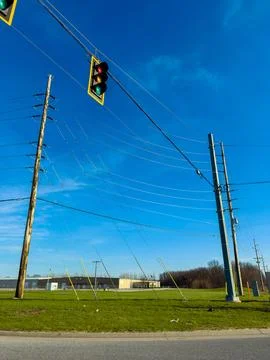 A traffic light hangs above a patch of green grass next to utility poles. Pow Stock Photos