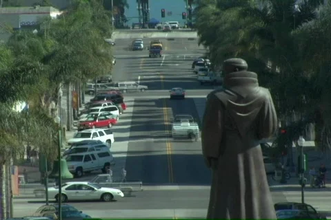 Traffic moves quickly on the streets adjacent to a statue of Junipero Serra. Stock Footage 339981