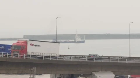 Traffic moving across a harbor bridge with a cargo ship sailing in the calm Stock Footage 346777073