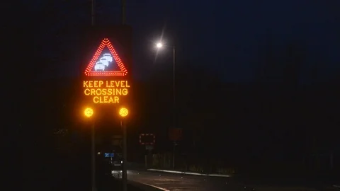 Traffic passing flashing keep level crossing clear warning sign at night uk Stock Footage 85598506