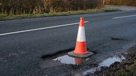 Traffic passing large pothole marked by warning traffic cone uk Stock Footage 85009438