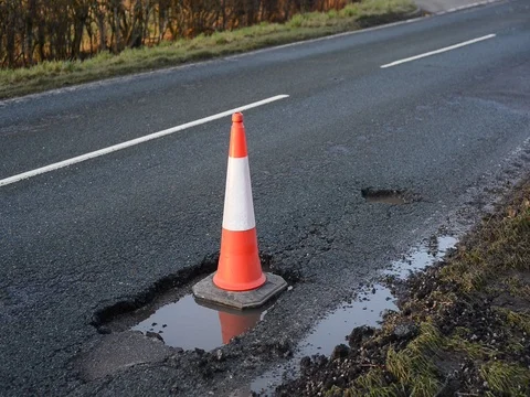 Traffic passing large pothole marked by warning traffic cone uk Stock Footage 85009549