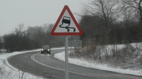 Traffic passing slippery road surface warning sign in snow united kingdom Stock Footage 20495631