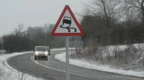 Traffic passing slippery road surface warning sign in snow united kingdom Stock Footage 20495694