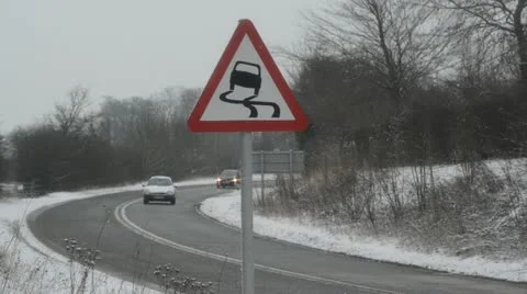 Traffic passing slippery road surface warning sign in snow united kingdom Stock Footage 20495774