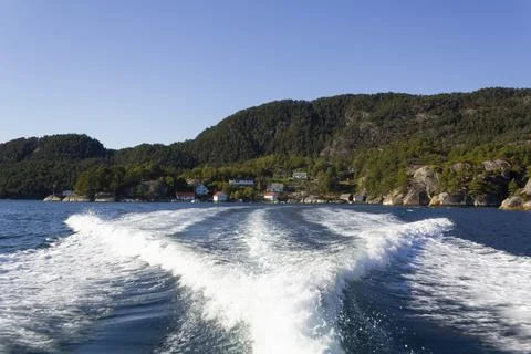 Trail on water surface of fast moving boat with norwegian houses on green for Stock Photos