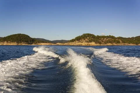 Trail on water surface of fast moving boat with norwegian green forest mounta Stock Photos