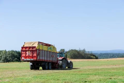 Trailer attached to a tractor is filled to the brim with freshly cut hay. Stock Photos