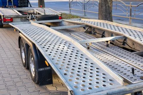 A trailer with a metallic surface is parked on a tree-lined street in the e.. Фото