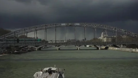 Train crossing bridge over La Seine river with dark clouds and rain in Stock Footage 142862486