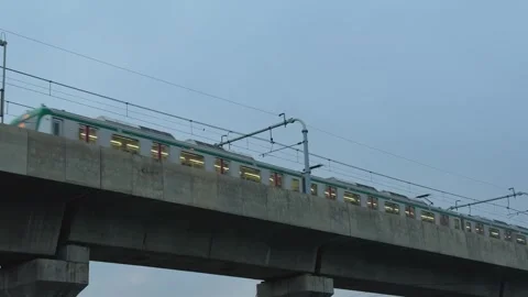 Train crossing a concrete bridge under a cloudy sky with visible overhead p.. Stock Footage 340056176