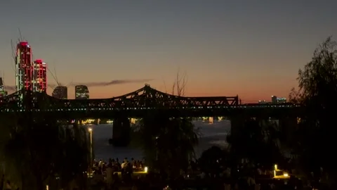 Train crossing illuminated bridge over river at sunset in modern city, evening Видео 337105040
