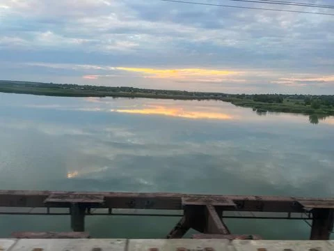 Train crossing river at sunset reflecting cloudy sky Stock Photos