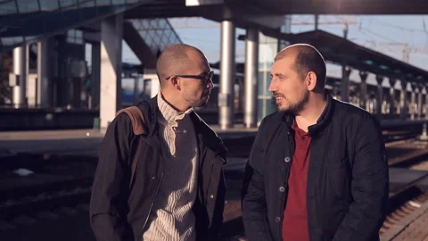 Train delay. Two men at sunset on the platform of the railway station looking at Stock Footage 99480196