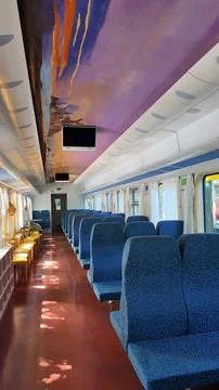 Train interior featuring rows of empty blue seats, a vibrant abstract ceiling Stock Photos
