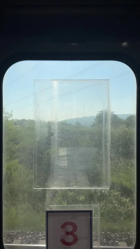 Train interior window, moving past verdant foliage, distant hill, railroad track Stock Footage 336189663