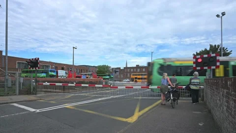 Train on level crossing after gates lowered with people &amp; vehicles waiting, UK Stock Footage 209593597