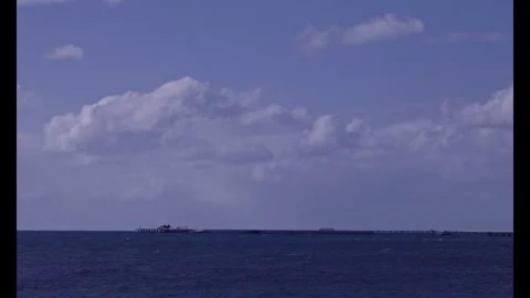 Train moves along end of long ocean jetty. Clouds sweep overhead on windy day Stock Footage 284312927