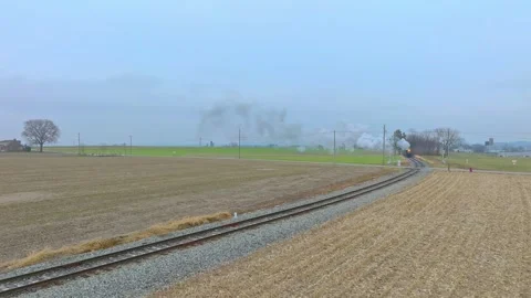 A train moves along the tracks in an open area. Fields surround the railway as Stock Footage 333722191