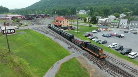 A train moves along the tracks in a small town. Parked cars fill the lot next Stock-Footage 338059745