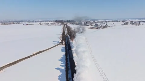 A train moves through a snow-covered area, clearing tracks as it goes. Snow Stock Footage 334315683