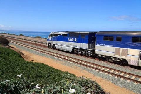 Train moving away from camera with Pacific Ocean in background Stock Photos