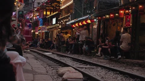 A train passes through Hanoi Train Street residents visitors sit close to tracks Stock Footage 330049523