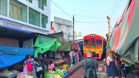 Train passing through vendors in Maeklong Railway Market with tourists Stock Footage 125523298