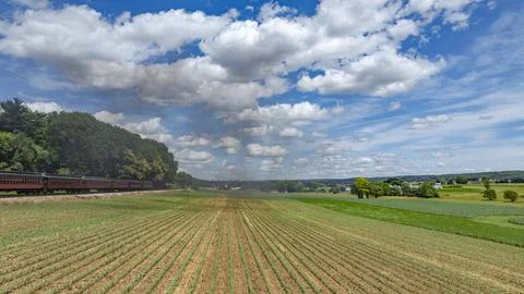 Train Passing Verdant Fields Under a Cloud-Filled Sky Stock Photos