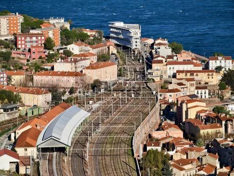 Train Progresses Past Colorful Rooftops Towards Bustling Seaside Terminal Under Stock Photos