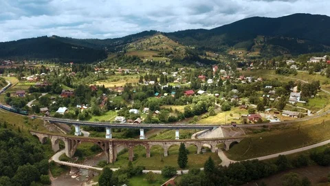 Train rides on old bridge viaduct among mountains and villages aerial drone view Stock Footage 116202532