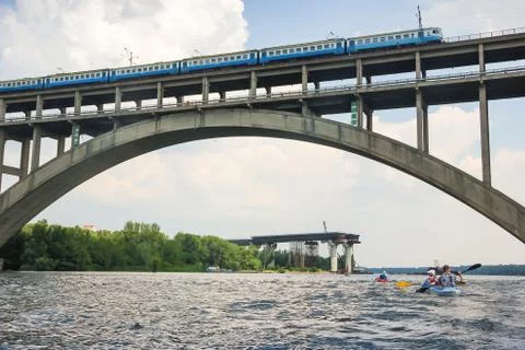 A train is riding over a bridge over a river against a blue sky Stock Photos