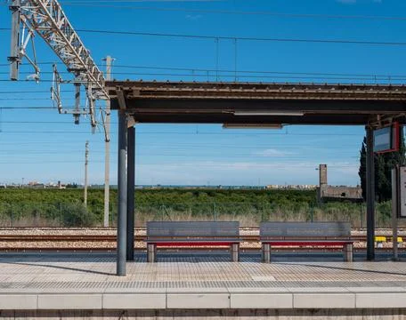 Train station platform features empty benches under metal awning. clear blue Stock Photos