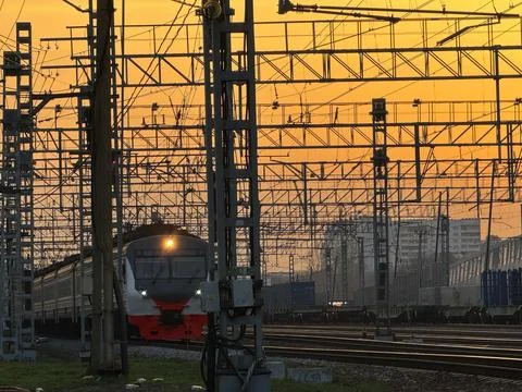 Train at sunset under intricate network of power lines Stock Photos
