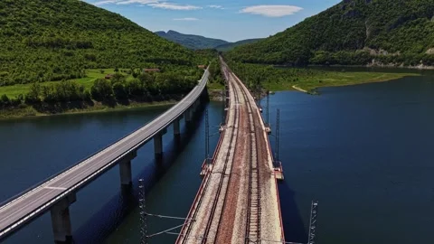 Train tracks curve along a river near mountains in bright sunlight Stock Footage 338276349